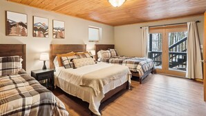 A cozy room with a wooden ceiling, a large bed, two smaller beds, a nightstand, a lamp, and a window with a view of trees. - Sunrise Dacha: 3  BR, 2.5  BA House in Canaan Valley, Sleeps 10 (Davis)