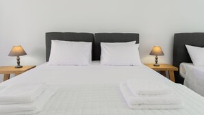 Una cama doble con ropa de cama blanca, dos mesitas de noche con lámparas y una pared lisa.