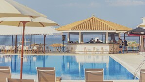 Zona de piscina con sillones de descanso y sombrillas, un bar y vistas al mar.