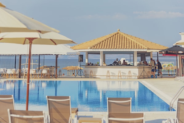 A pool area with lounge chairs and umbrellas, a bar, and a view of the sea. - LA PLAYA GRANDE (Corfu)