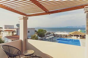 A balcony with a view of a swimming pool, lounge chairs, and a beach area. - LA PLAYA GRANDE (Corfu)
