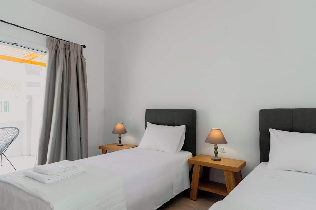 Una camera d'albergo con due letti, una finestra con tende e due lampade da comodino.
