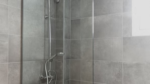 A glass-enclosed shower stall with a handheld showerhead and a wall-mounted faucet.