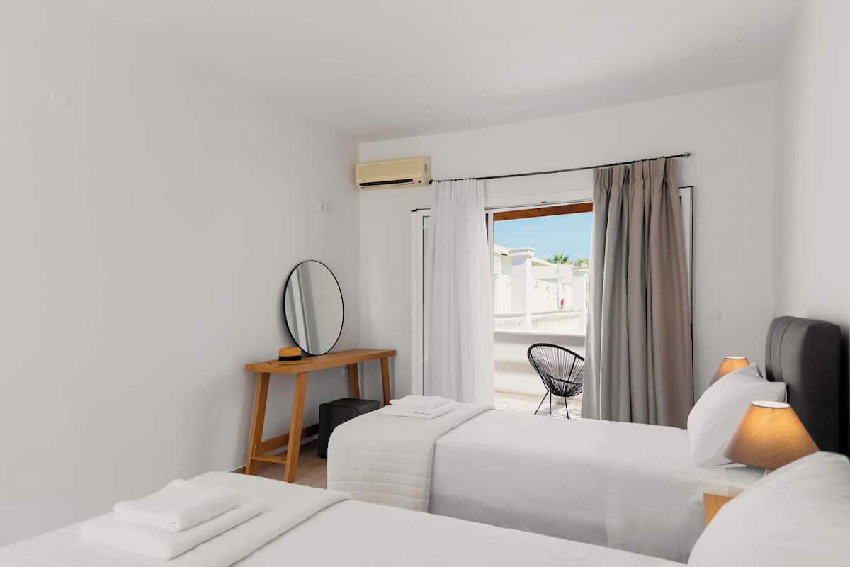 Camera d'albergo con due letti, un tavolino in legno, una sedia e vista esterna.