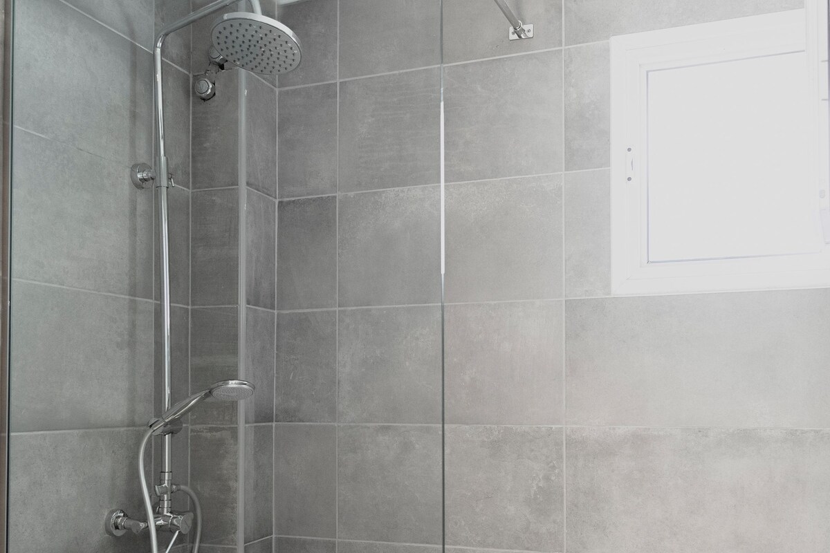 A glass-enclosed shower stall with a handheld showerhead and a wall-mounted faucet.