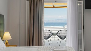 Una habitación de hotel con una cama, una mesita de noche con lámpara y vista a la playa a través de una ventana con cortinas.