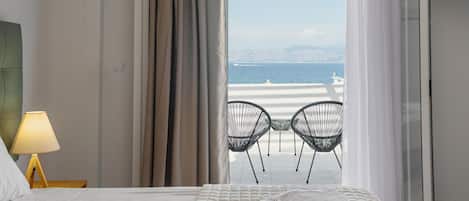 Une chambre d’hôtel avec un lit, une table de chevet avec une lampe et une vue sur la plage, visible à travers une fenêtre munie de rideaux.