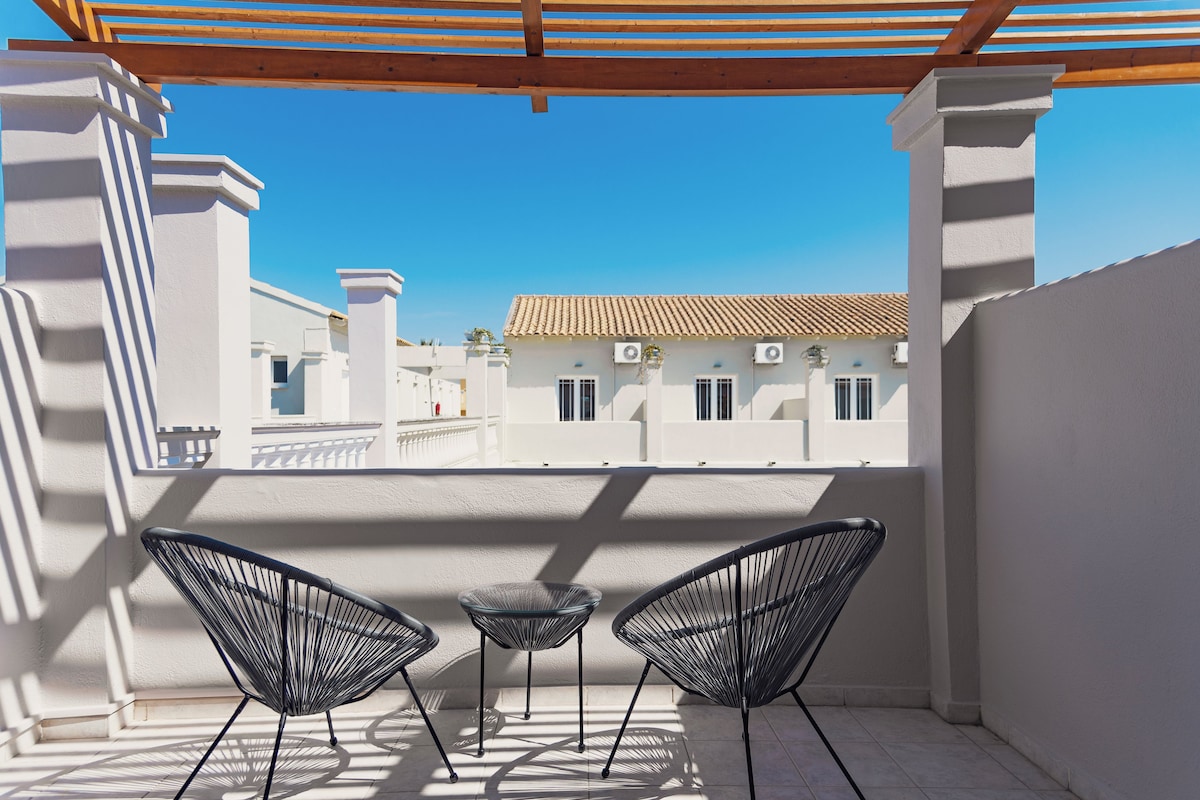 Un balcon avec deux chaises en fil de fer noir et une petite table, donnant sur un immeuble dont le toit est recouvert de tuiles.