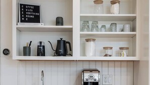 A kitchen with white cabinetry, a coffee maker, and various storage jars. - Tate House (Saugatuck)