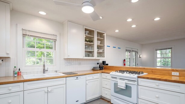 A modern kitchen with white cabinets, a built-in oven, and a window with blinds. - Tate House (Saugatuck)