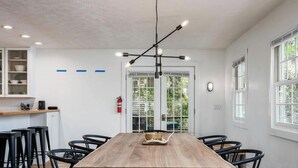 A modern dining area with a wooden table, black chairs, and a unique pendant light fixture. - Tate House (Saugatuck)