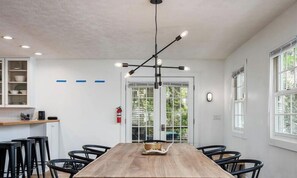 A modern dining area with a wooden table, black chairs, and a unique pendant light fixture. - Tate House (Saugatuck)