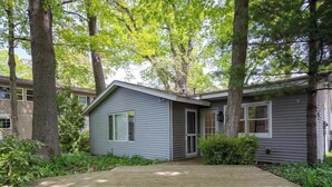 A single-story house with a front deck, surrounded by trees and greenery. - Tate House (Saugatuck)