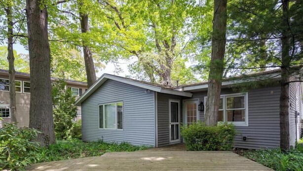 A single-story house with a front deck, surrounded by trees and greenery. - Tate House (Saugatuck)
