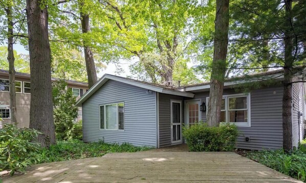 A single-story house with a front deck, surrounded by trees and greenery. - Tate House (Saugatuck)