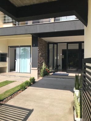 A modern building with a covered entrance, a glass door, and a concrete pathway. - Apart Hotel Encantos do Mar  (Palhoça)
