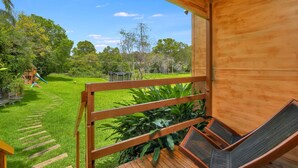 A wooden deck with a view of a grassy yard and playground equipment.