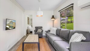 A modern living room with a grey sofa, a small armchair, a coffee table, and a large window with a view of greenery.