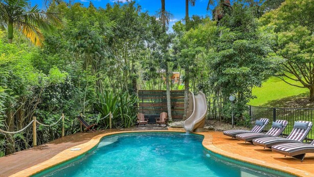 A swimming pool with lounge chairs and a slide, surrounded by lush greenery.