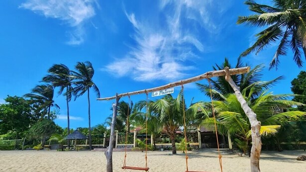 A beach with two swings made of wood and ropes, palm trees, and a clear blue sky. - Le Palme Beach Resort (Pandan)