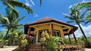 A small, single-story building with a brown roof and yellow walls, surrounded by palm trees and tropical plants. - Le Palme Beach Resort (Pandan)