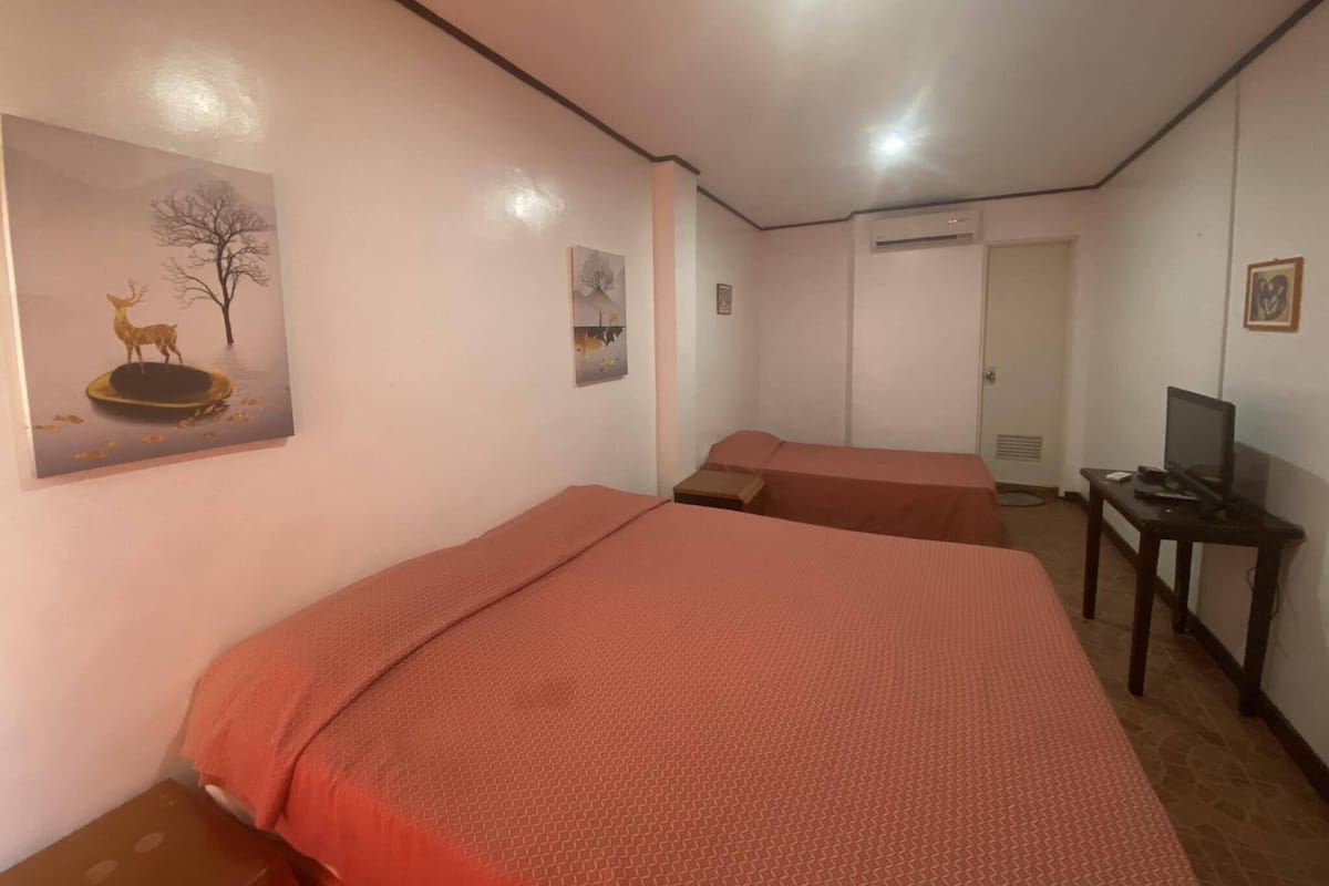 Quarto de hotel com duas camas, uma escrivaninha, televisão e obras de arte nas paredes.