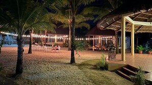A beachfront property with a covered outdoor seating area, palm trees, and string lights. - Le Palme Beach Resort (Pandan)