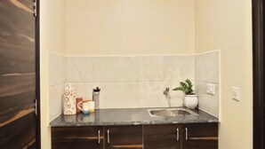 A small, modern kitchen with dark wooden cabinets, a marble countertop, and a single sink. - Covie Gurgaon 70 (Gurugram)