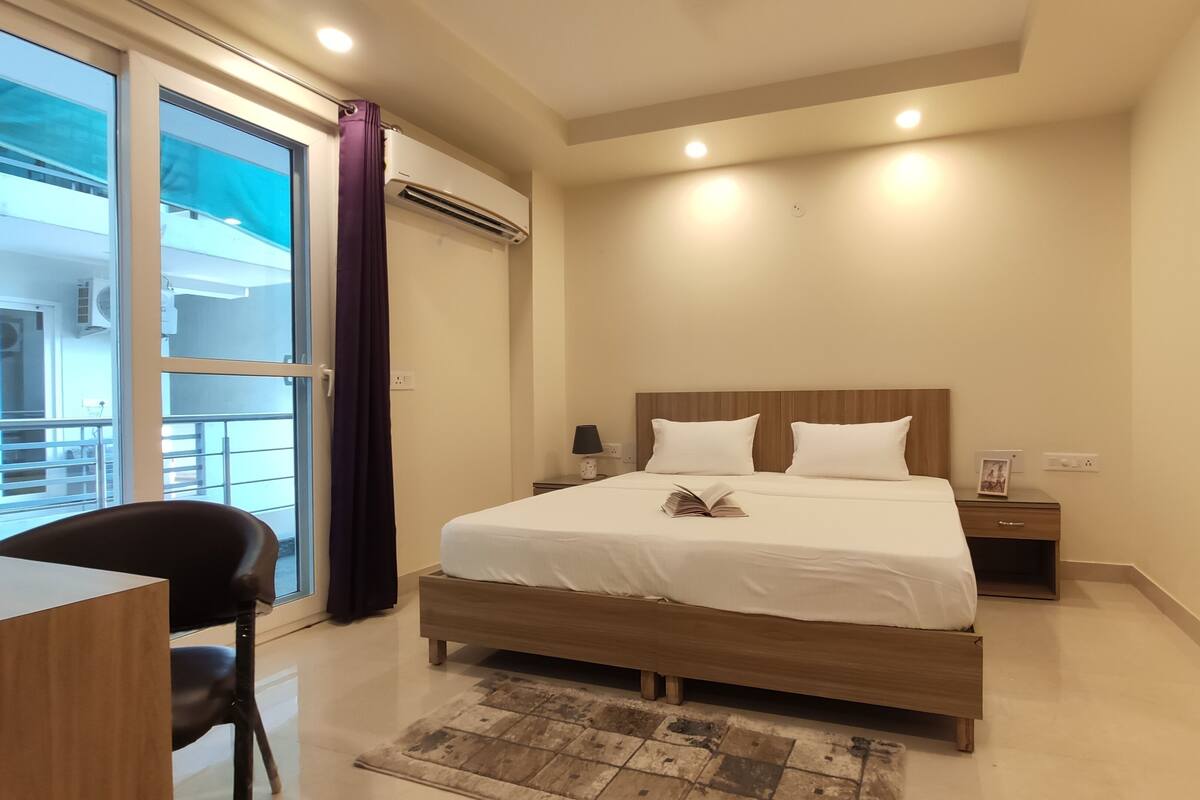 Habitación de hotel con cama, mesita de noche, lámpara y vistas al balcón exterior.