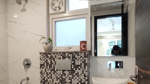 A modern bathroom with a white toilet, a black and white mosaic sink vanity, and a shower with a handheld showerhead. - Covie Gurgaon 70 (Gurugram)