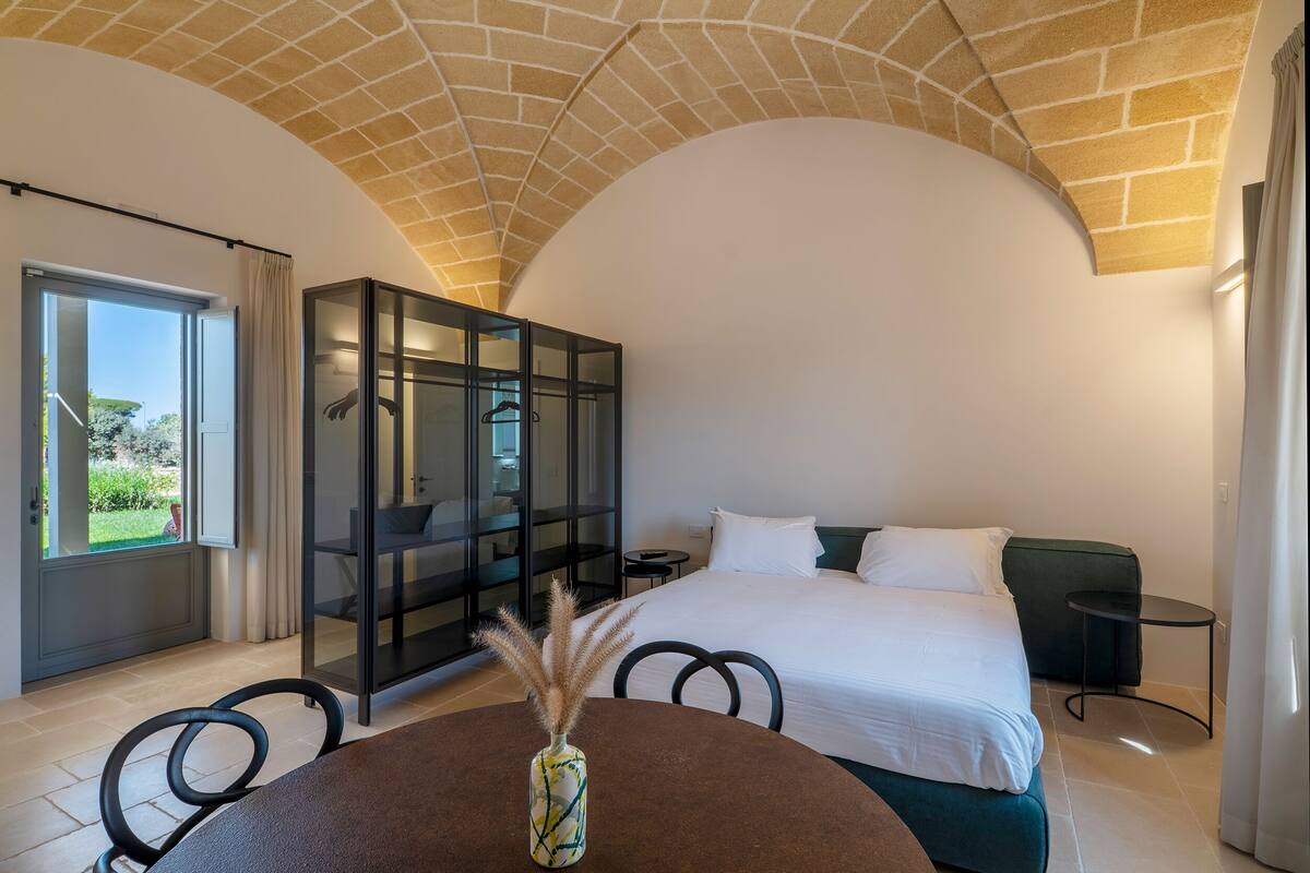 Un dormitorio con cama, un aparador de vidrio, una mesa de comedor con sillas y vistas al exterior.