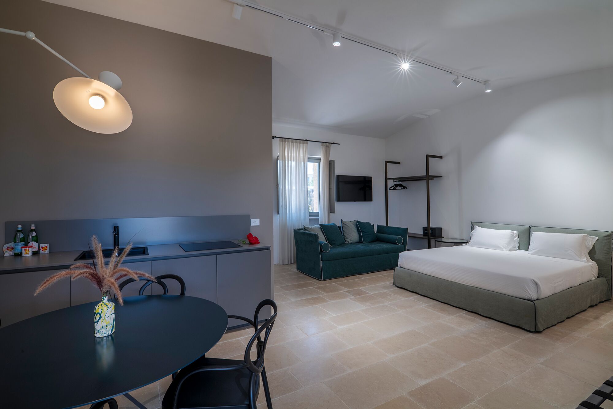 A modern hotel room with a bed, a sofa, a dining table, and a TV.