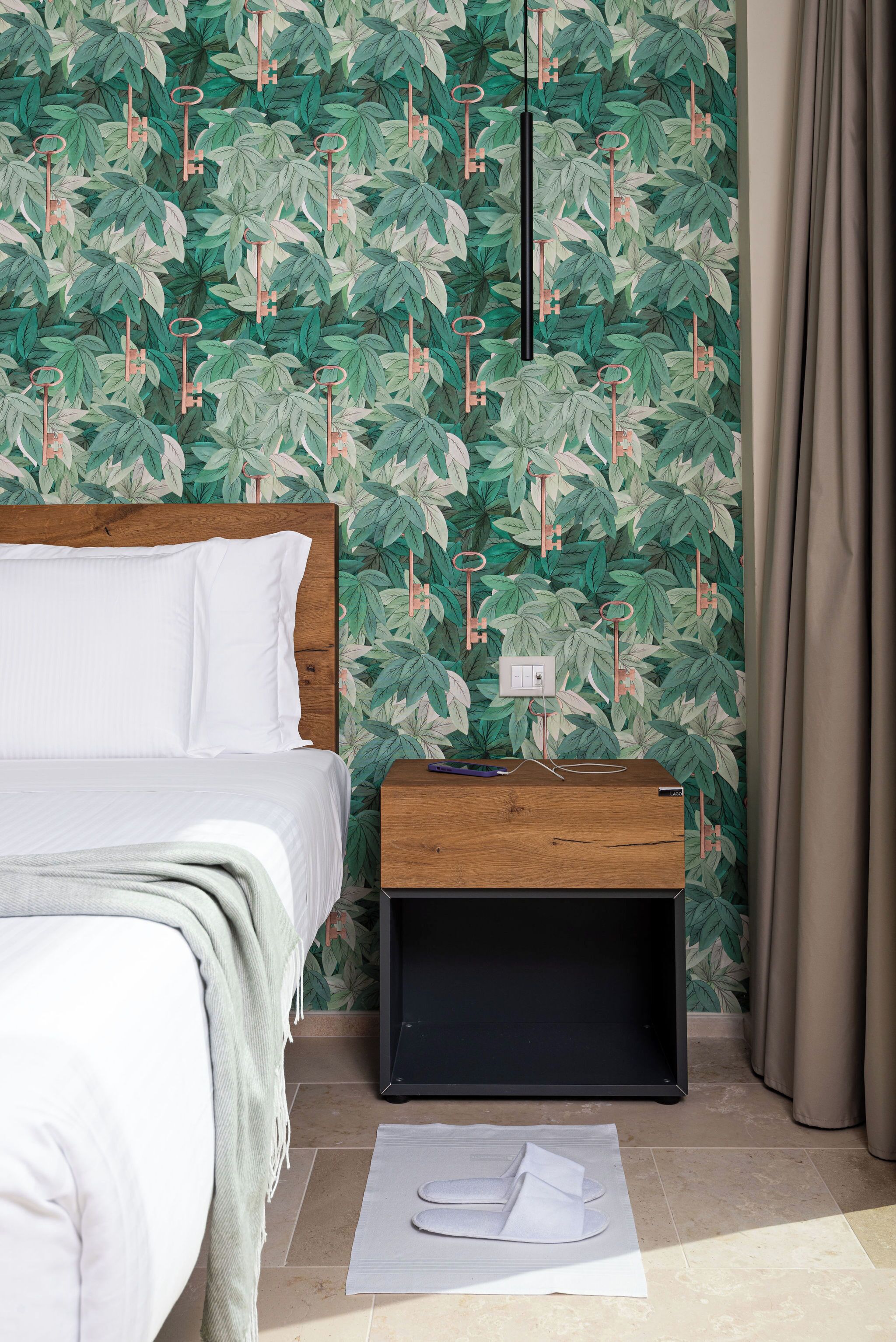 A bedroom with a bed, a nightstand, and a wall with a leafy pattern.