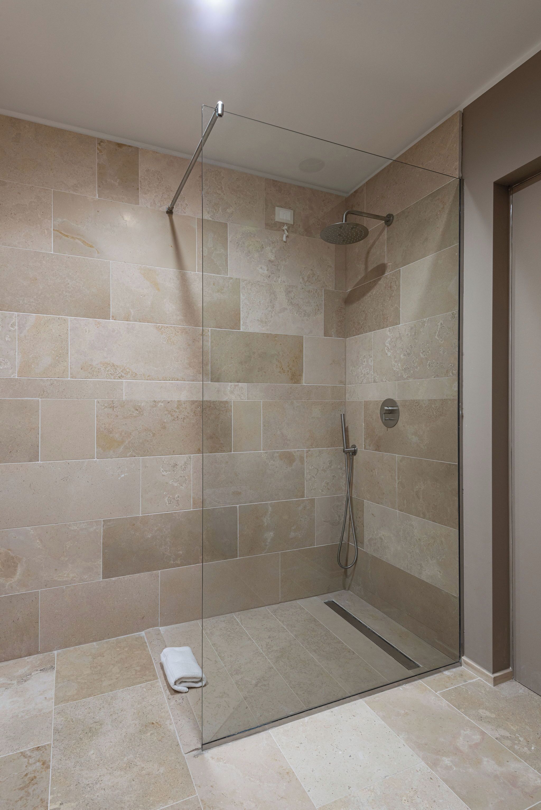 Une douche fermée par des parois de verre, avec des carreaux de couleur beige et une porte en verre.