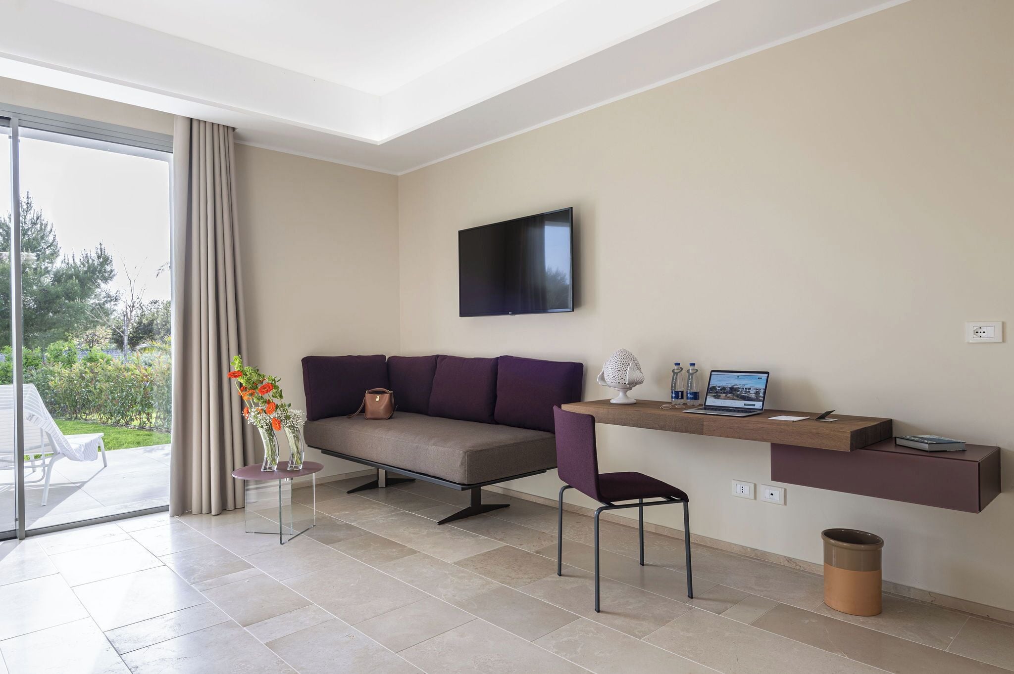 Un salon moderne avec un canapé, un fauteuil, un téléviseur et un ordinateur portable posé sur une étagère intégrée.