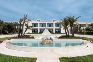 A modern hotel with a central pool, palm trees, and a well-maintained garden.