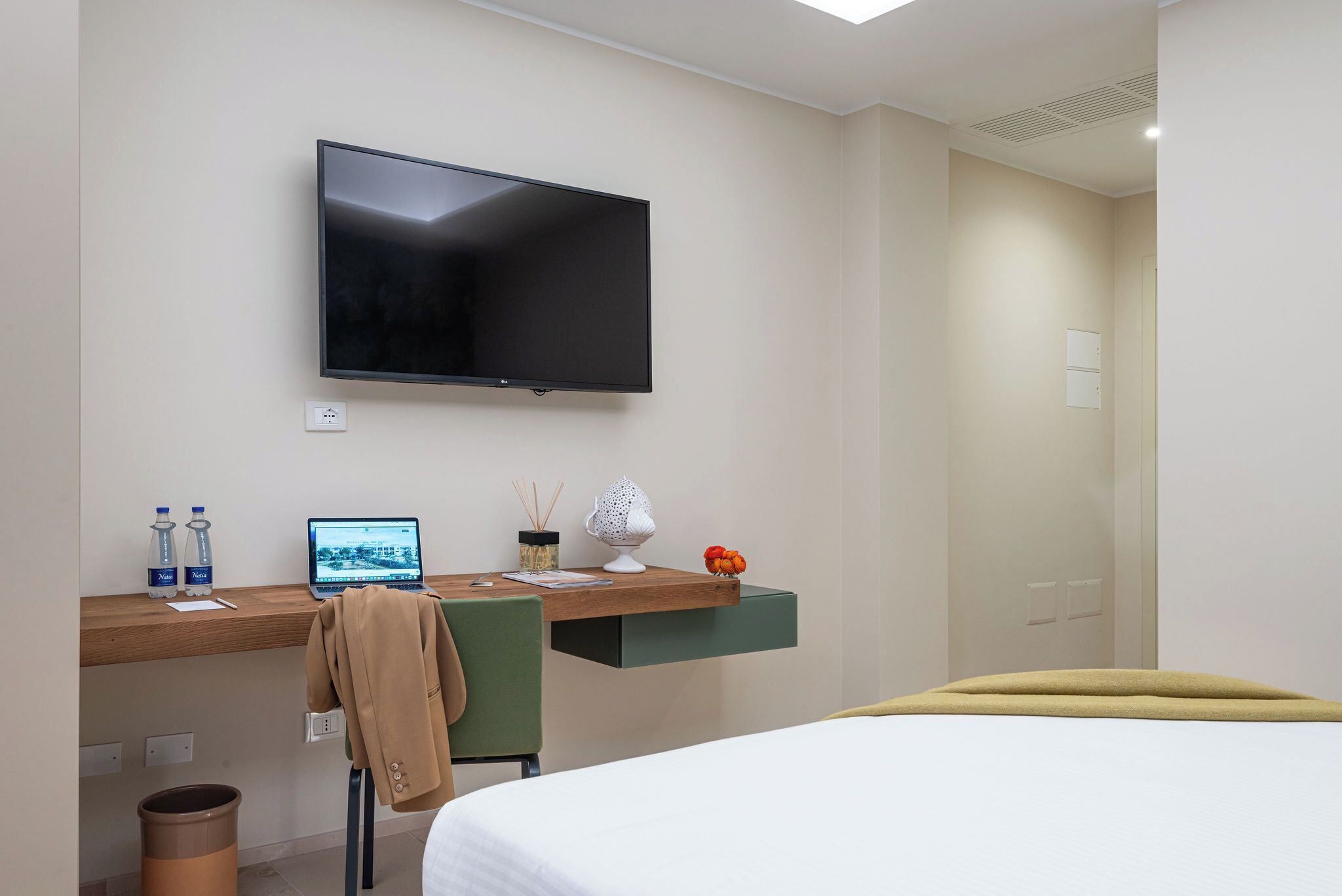 Une chambre d’hôtel comprenant un lit, un bureau avec un ordinateur portable, une télévision et une petite étagère avec des objets décoratifs.