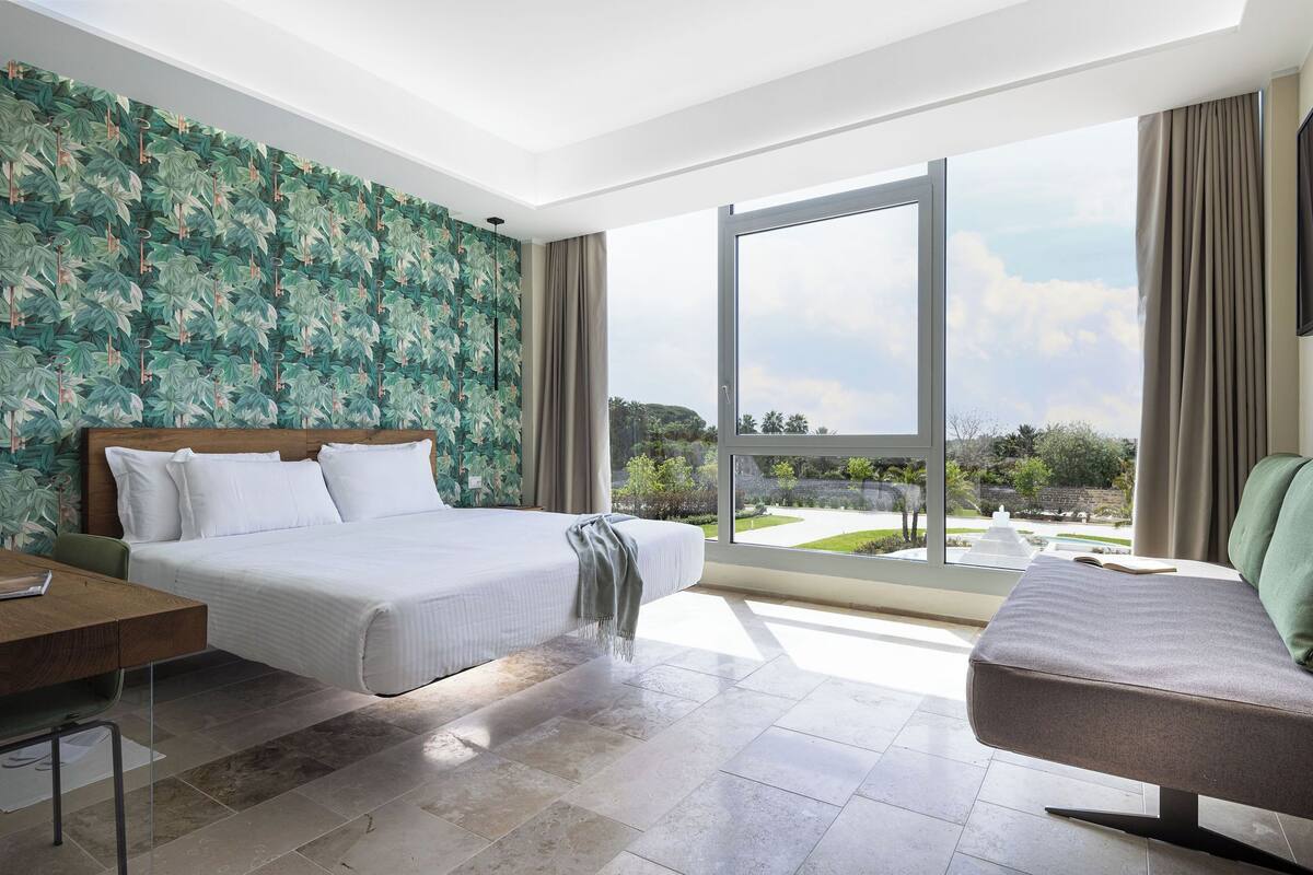 Una habitación de hotel moderna con una cama grande, un escritorio y vistas al exterior.
