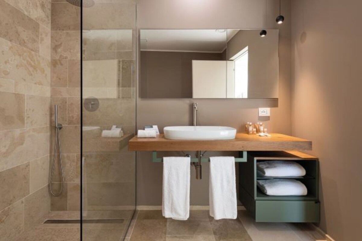 Un baño moderno con cabina de ducha de vidrio, tocador de madera, espejo grande y toallero.