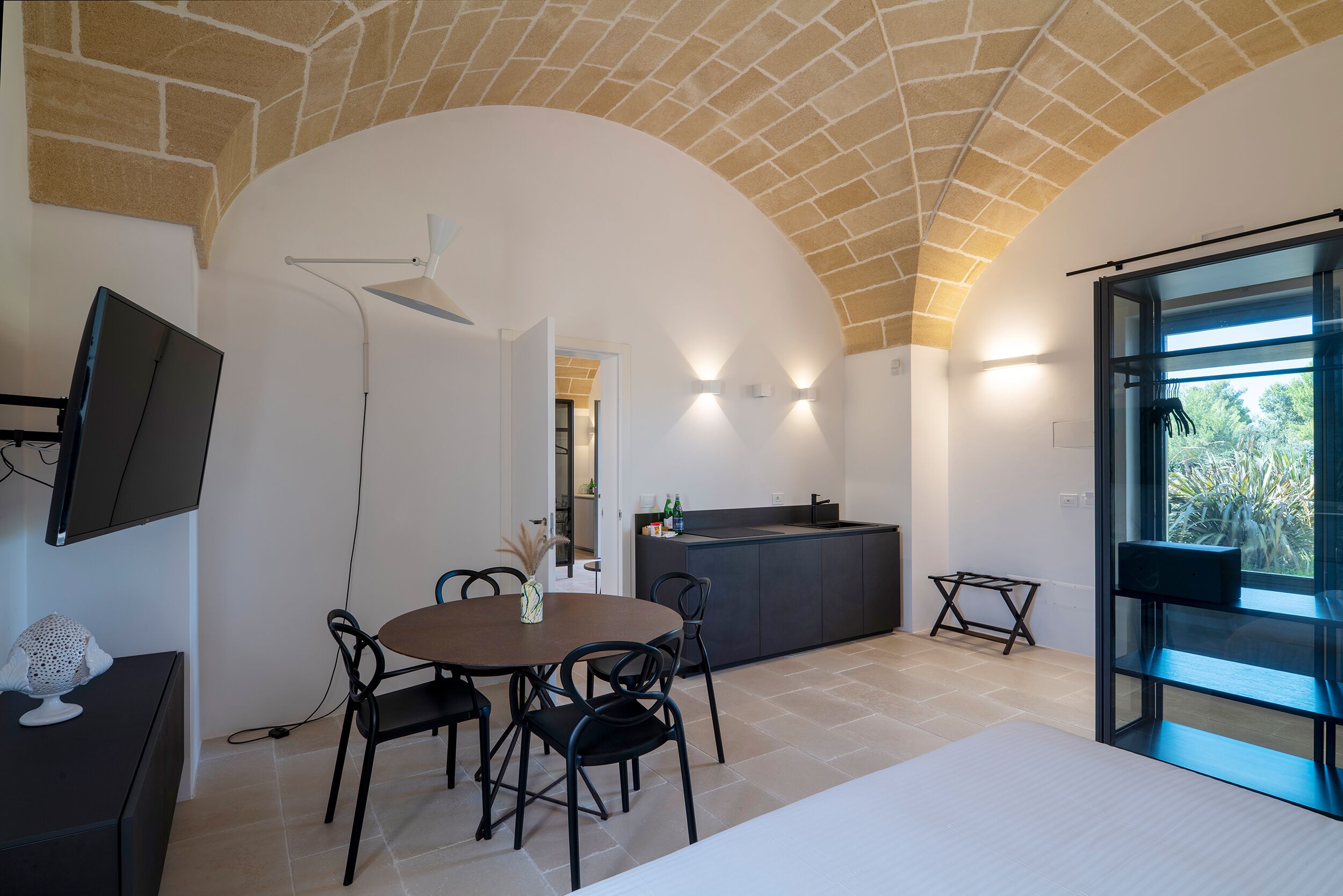 A modern kitchen with a curved ceiling, a dining area with a round table and chairs, and a large window providing a view of the outdoors.