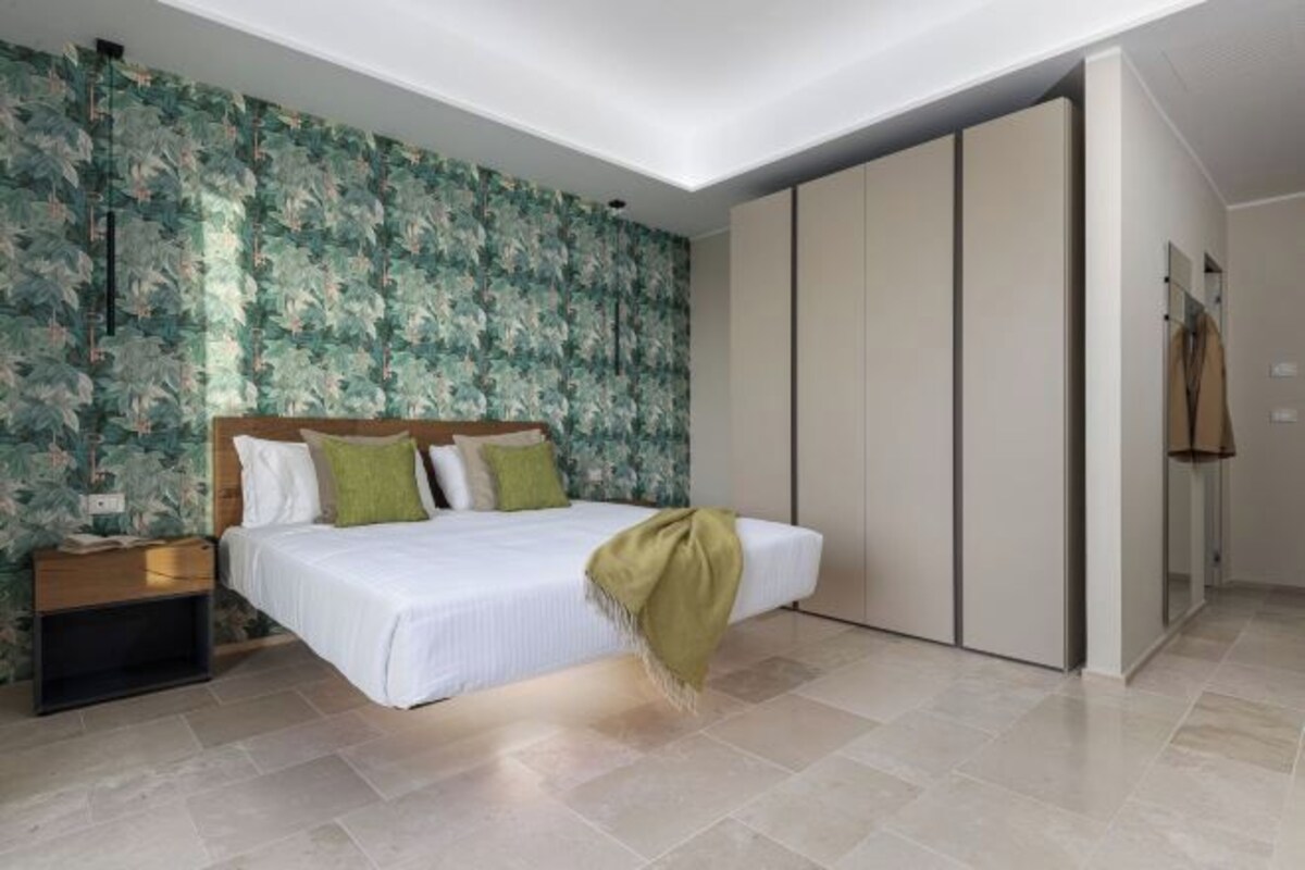 Un dormitorio con cama, mesita de noche, armario y una pared con estampado floral.