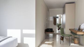 A modern hotel room with a bed, a desk, a chair, and a wardrobe.