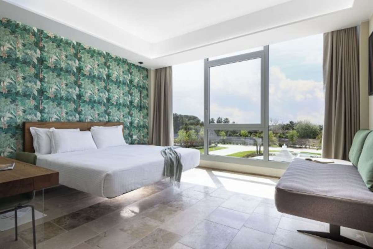 Una habitación de hotel moderna con una cama grande, un escritorio y vistas a un jardín ajardinado a través de un ventanal corredero.