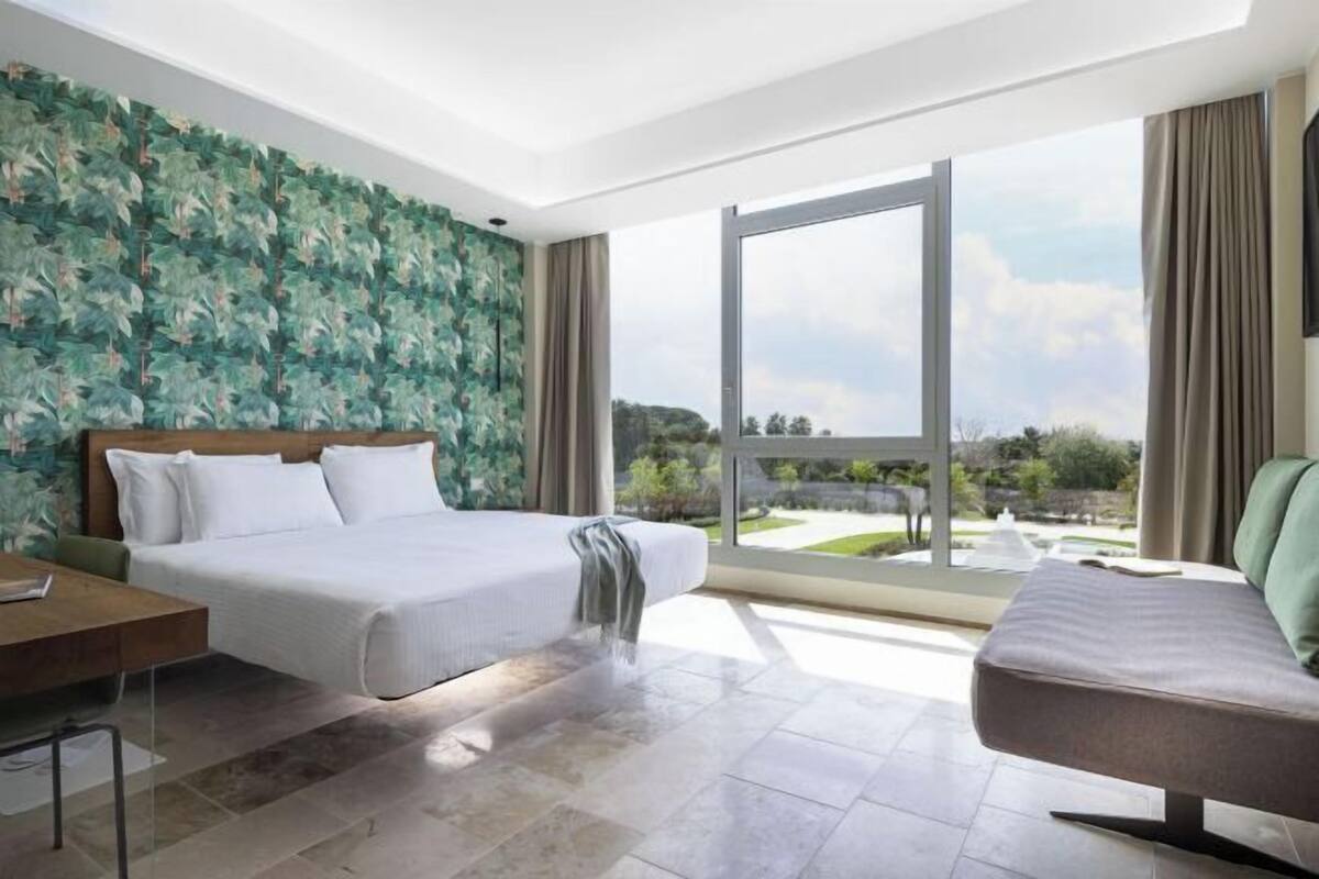 Una habitación de hotel moderna con una cama grande, un escritorio y vistas a un jardín ajardinado a través de un ventanal corredero.
