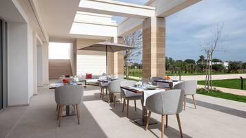 An outdoor dining area with a modern patio, multiple tables and chairs, and a view of the surrounding landscape.