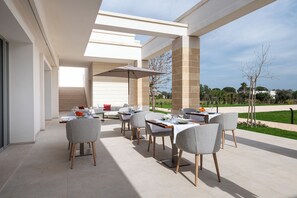 An outdoor dining area with a modern patio, multiple tables and chairs, and a view of the surrounding landscape.