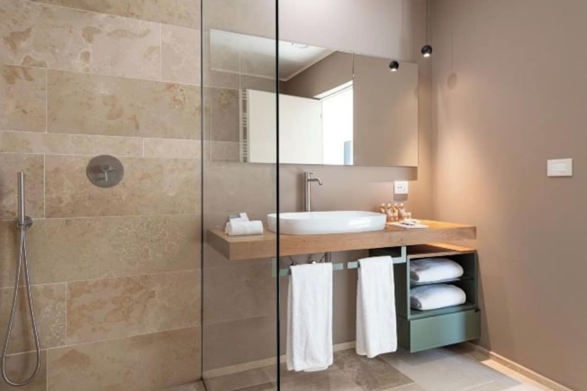 Un baño moderno con ducha envuelta en vidrio, un espejo grande y un mueble de tocador de madera con lavabo y espacio para toallas.