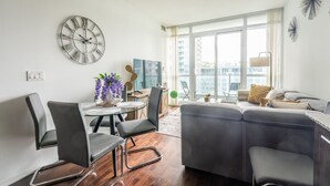 A modern living room with a grey sofa, two black chairs, a round table with a vase of purple flowers, and a large wall clock. - GLOBALSTAY. Bright 1Br+Den Unit in Downtown (Toronto/Canada)