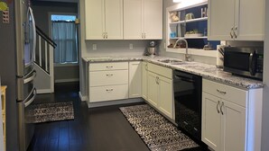 Una cocina moderna con armarios blancos, encimera de granito, microondas integrado y refrigerador de acero inoxidable.