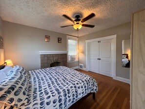 A bedroom with a bed, a ceiling fan, a fireplace, and a wardrobe.